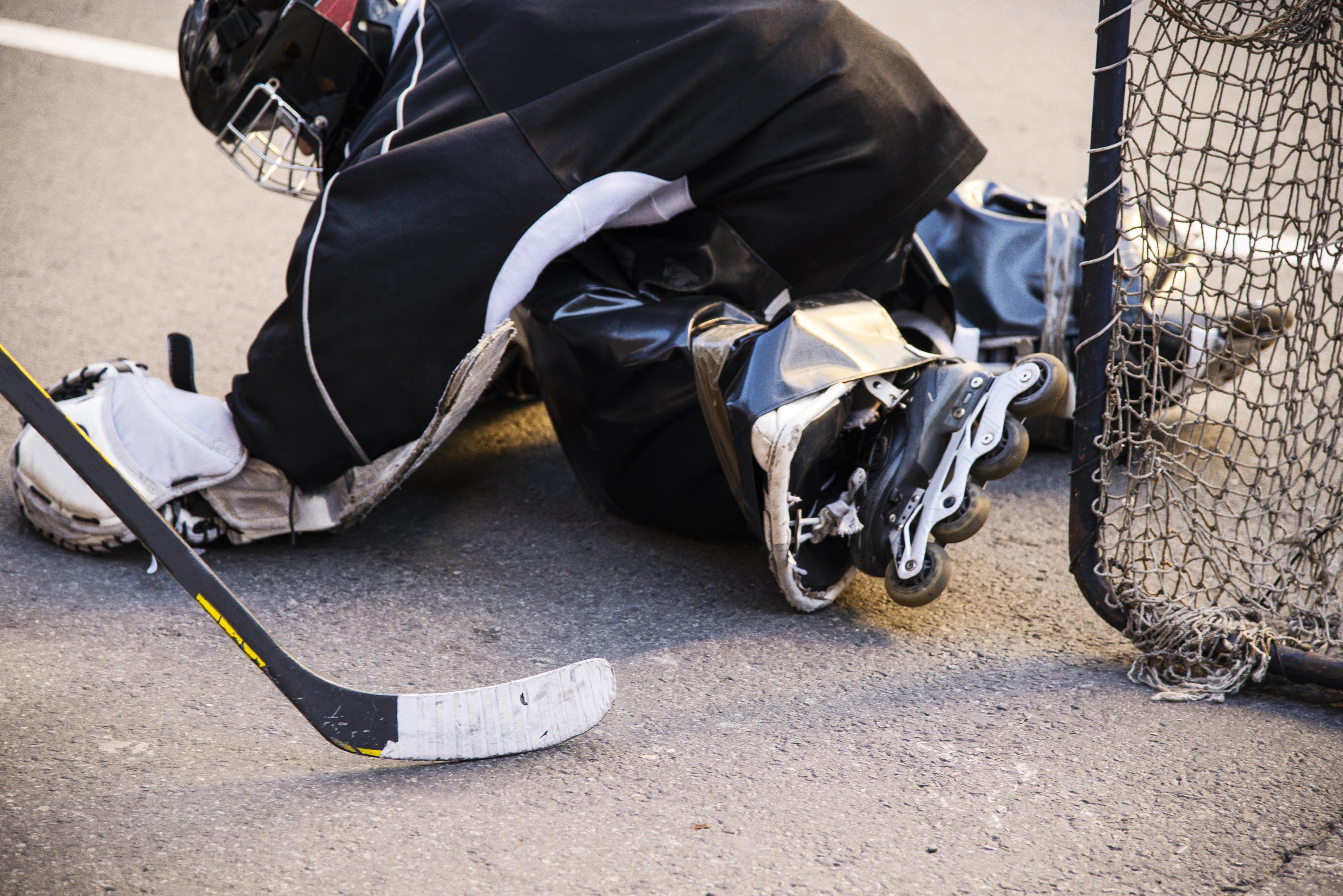 kid playing street hockey on rollerblades in full goalie gear