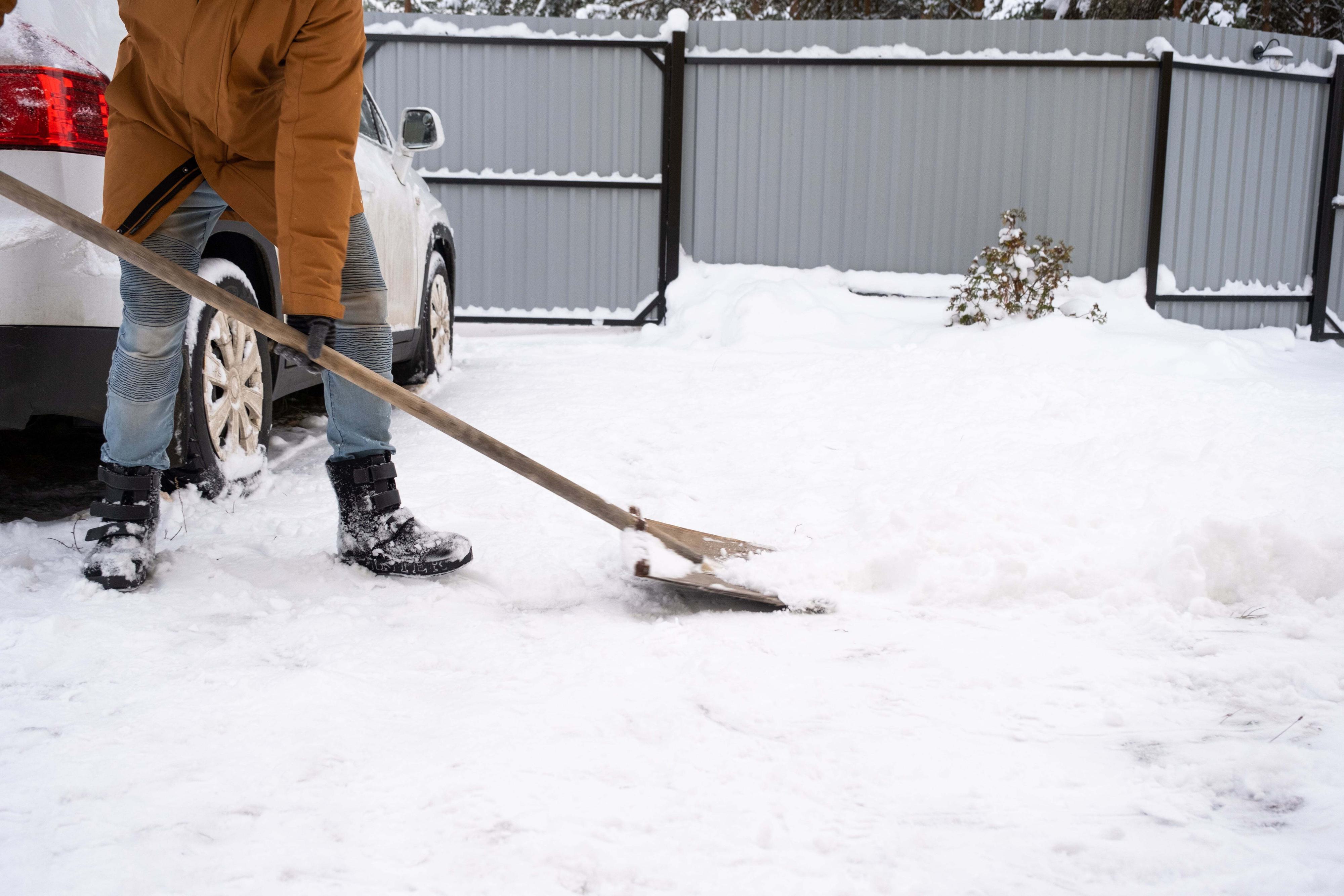 A man clears snow on driveway between gate and garage door