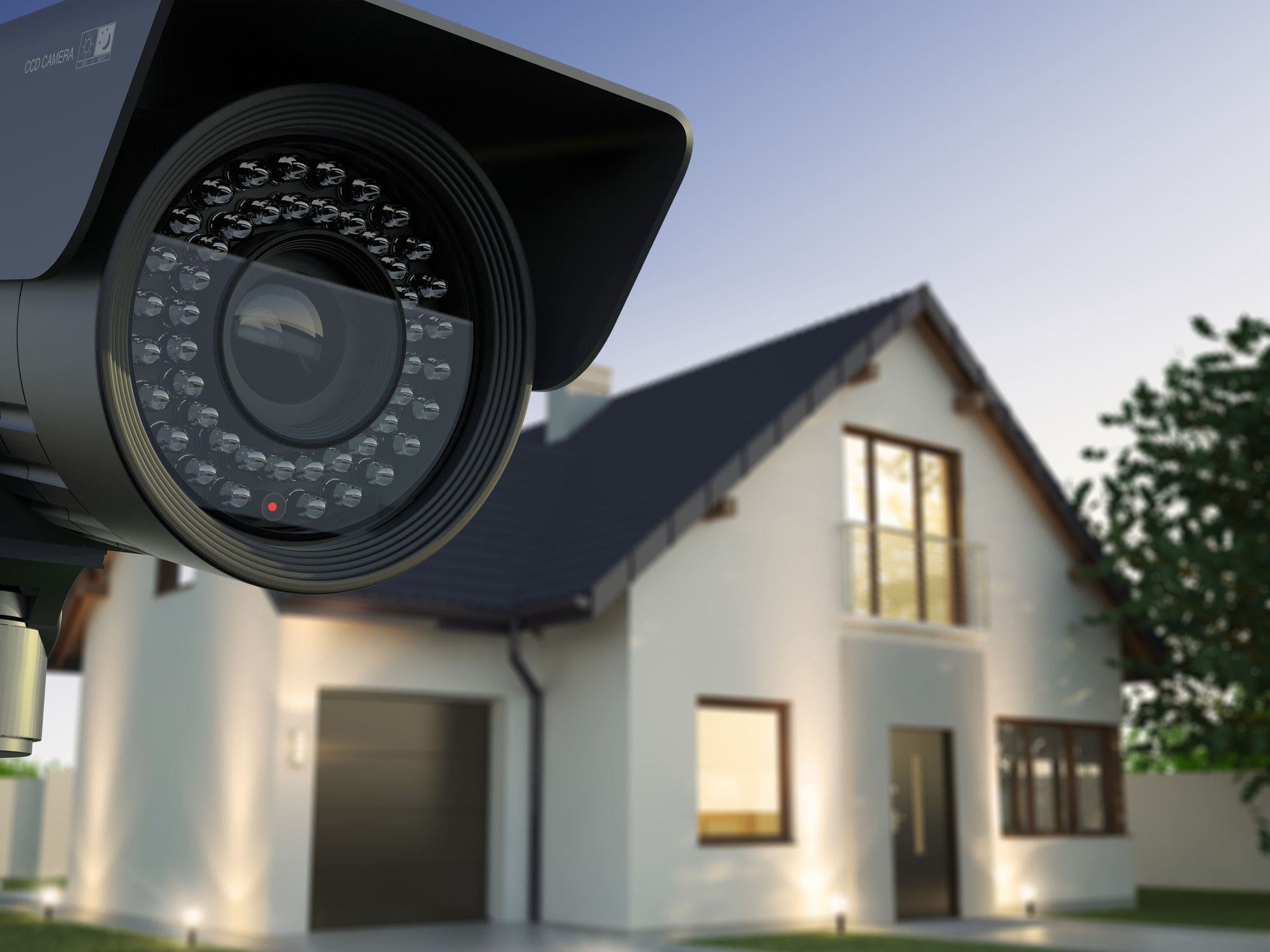 black CCTV security camera fixed to driveway gate of home at night