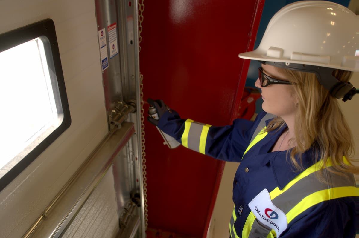 Creative Door Services technician lubricating commercial sectional door rollers and tracks