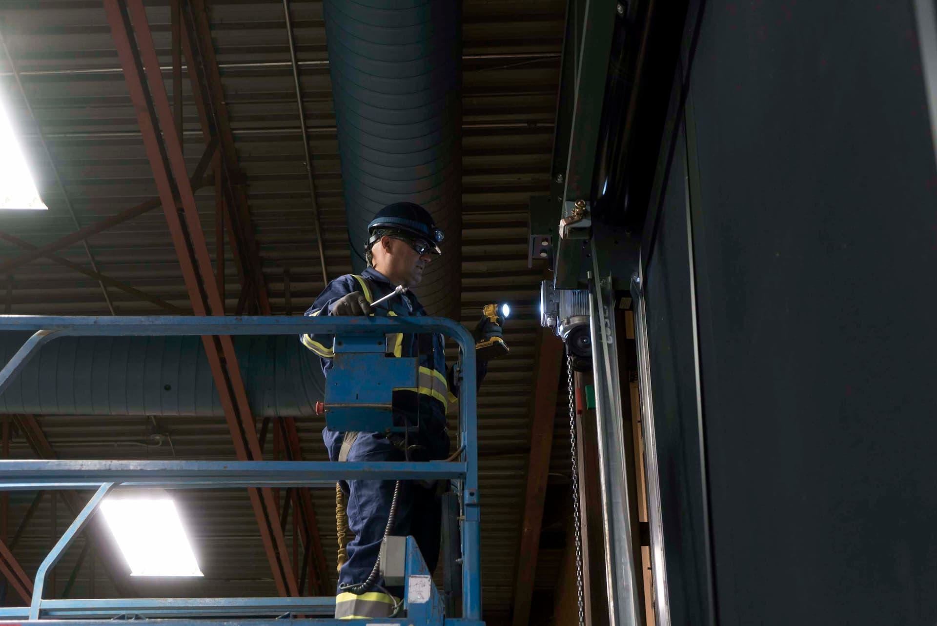 Creative Door technician on lift inspecting commercial sectional door with flashlight