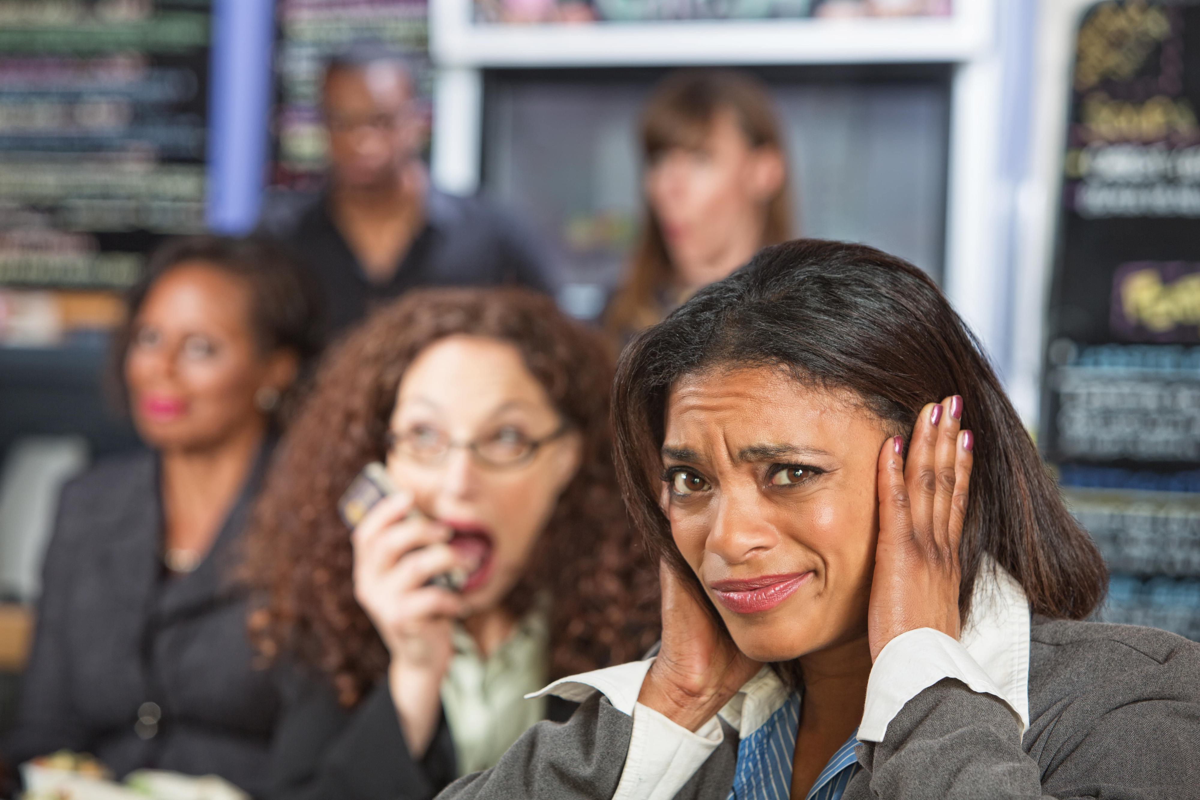 Business woman in a busy commercial setting covering ears