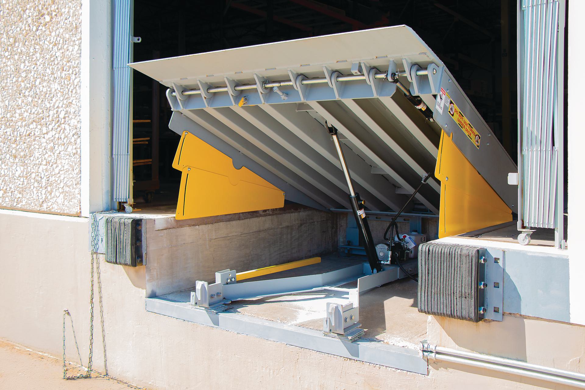 Hydraulic dock leveler raised for inspection, showing mechanical parts needing maintenance