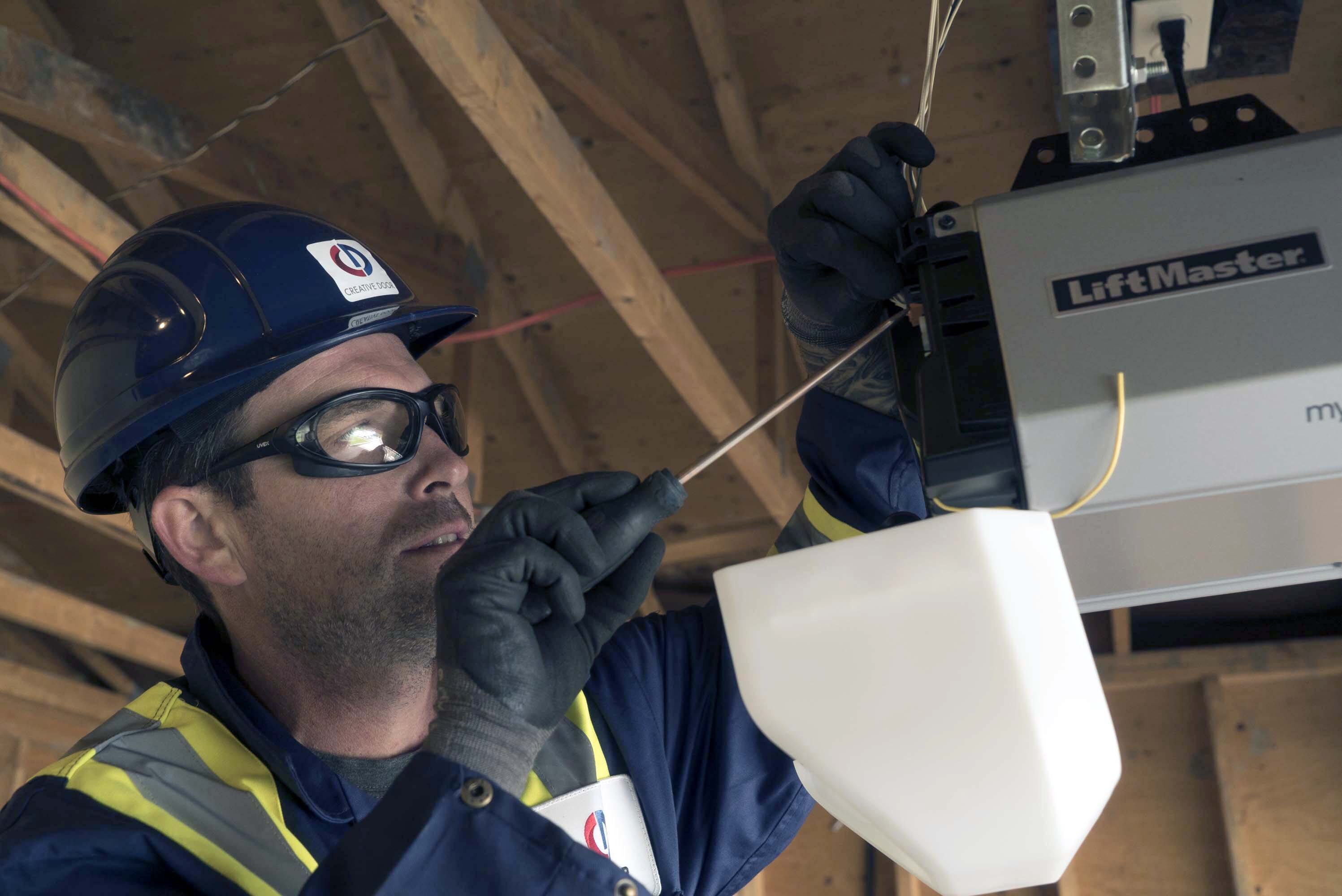 Creative Door Services technician repairing a garage door opener using a screwdriver