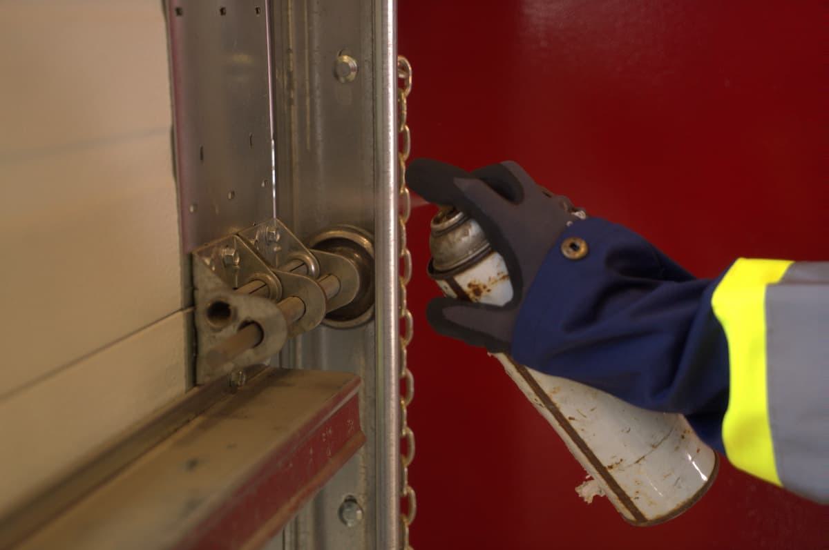 Technician performing maintenance and lubricating garage door hinge