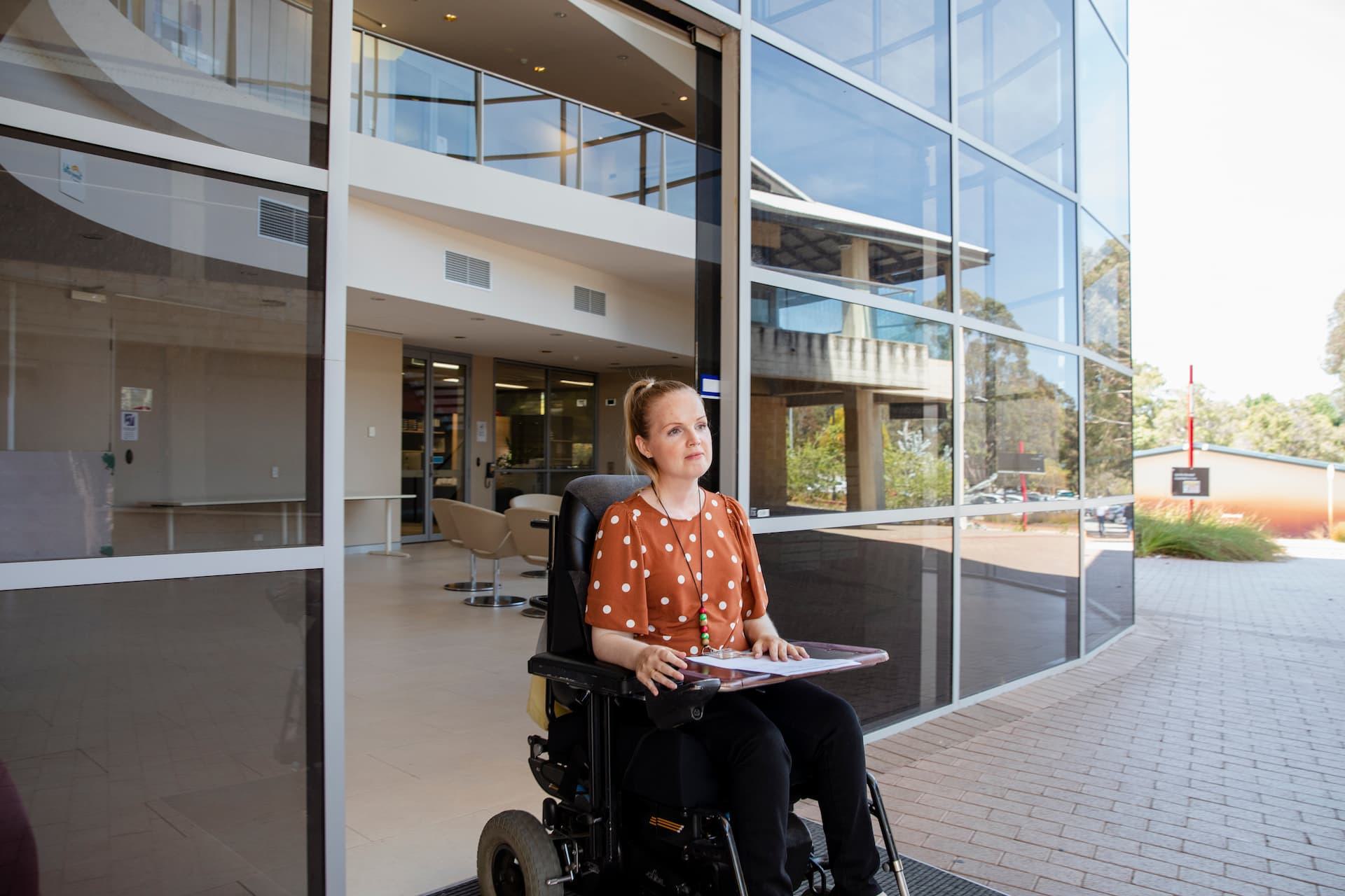 Woman in a wheelchair outside a building with automatic hands-free pedestrian doors