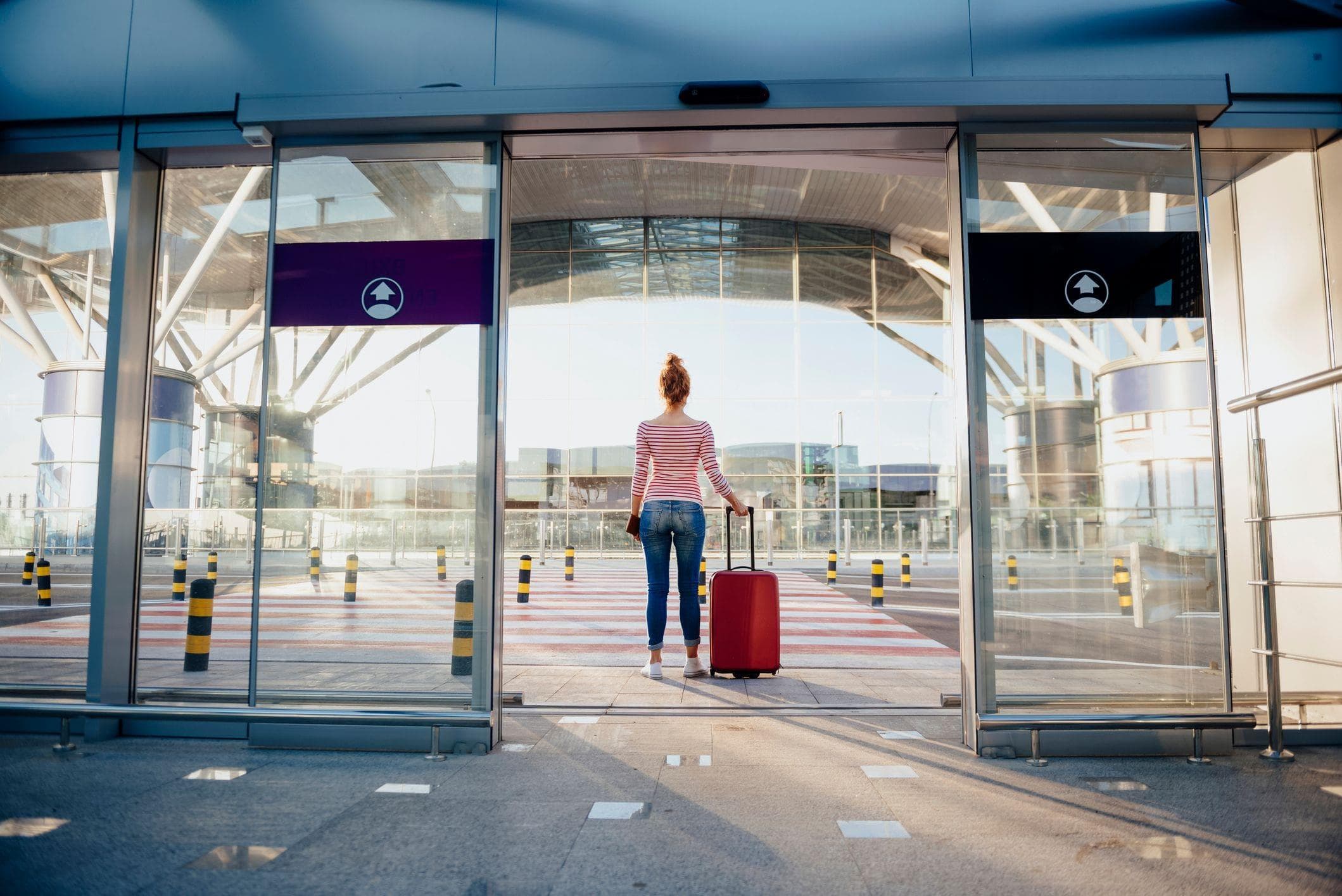 woman standing with suitcase in front of high traffic automatic glass doors
