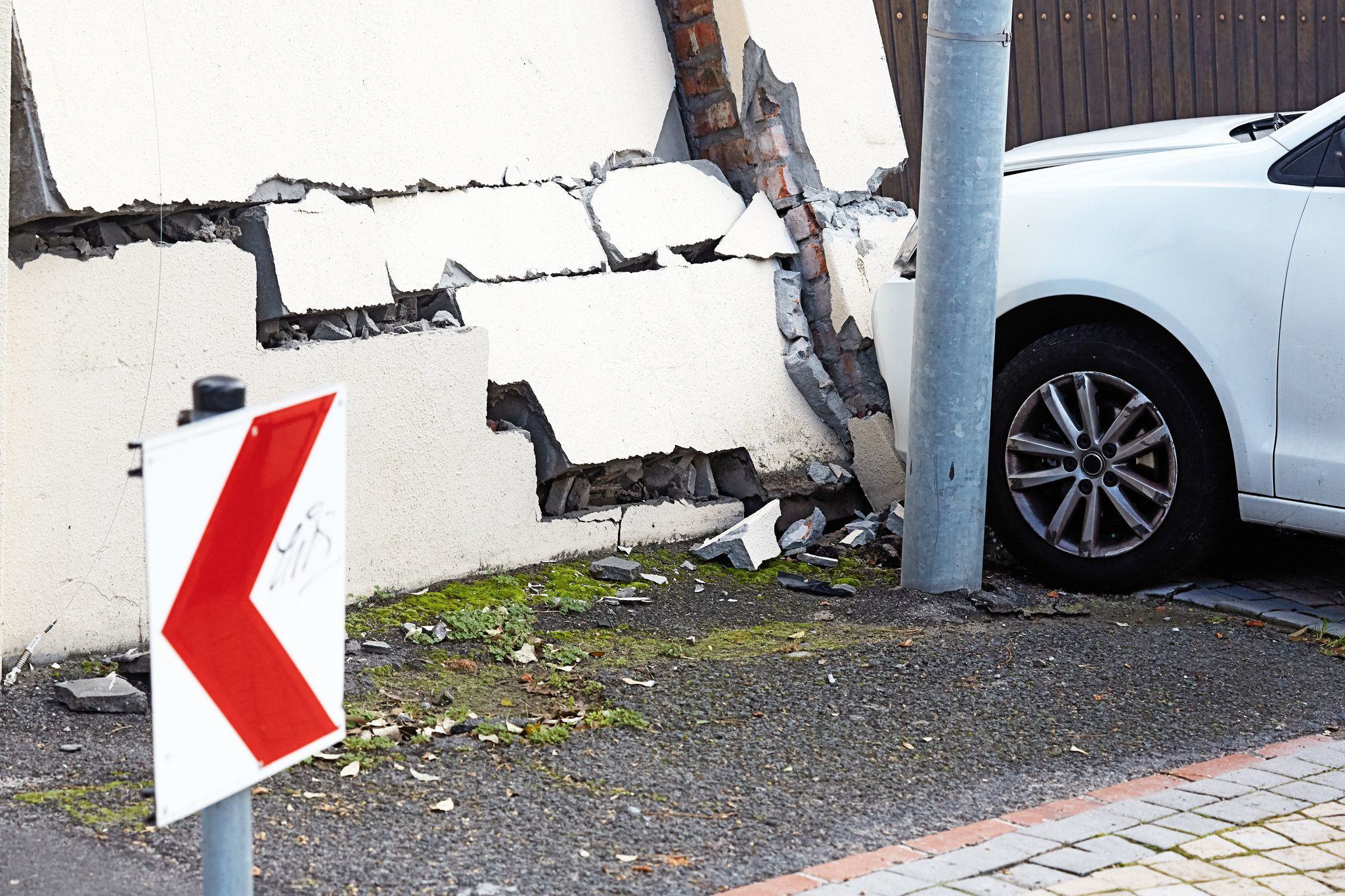 a white car that has driven in to a driveway gate and concrete pillar