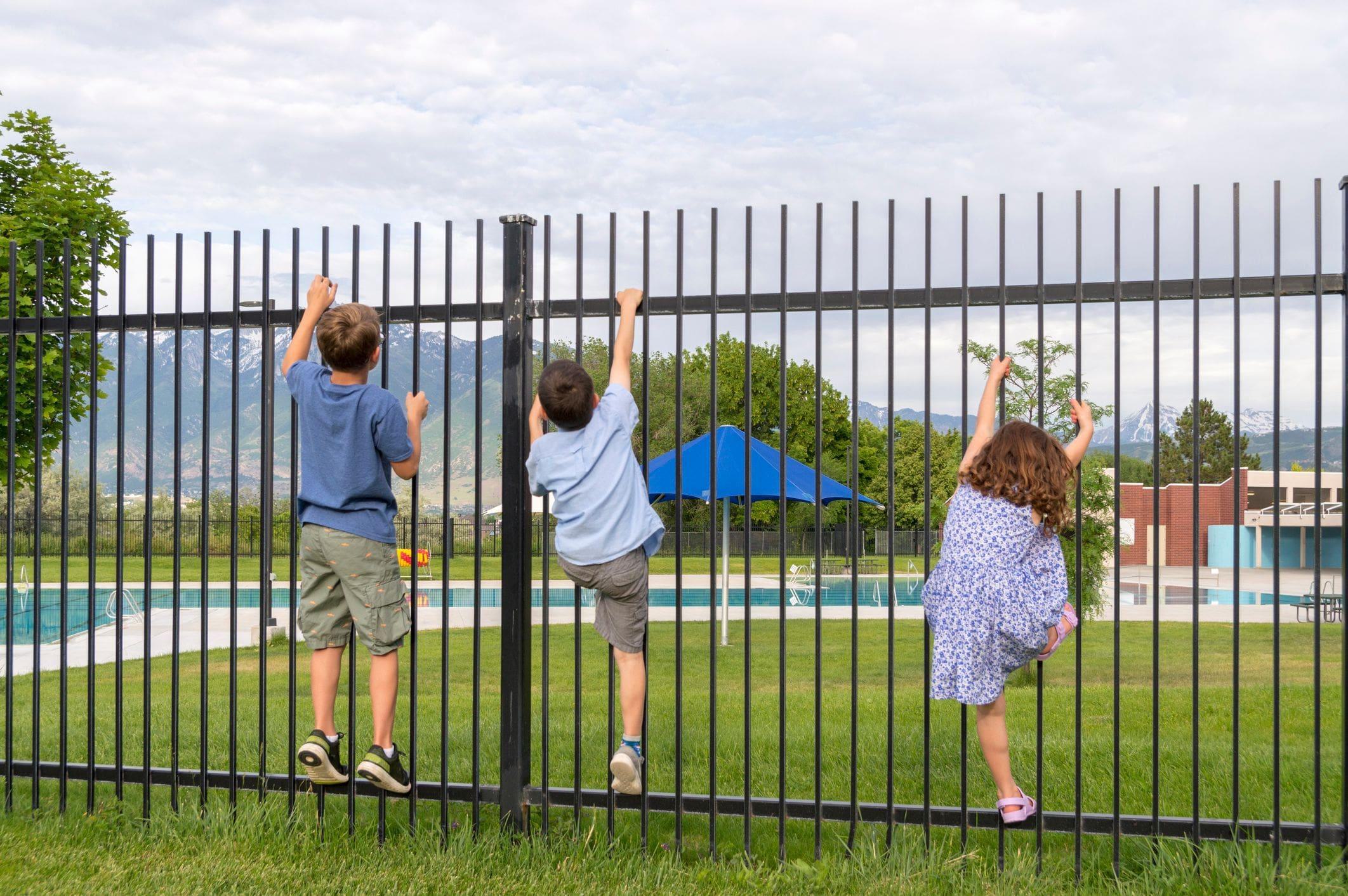 children trying to climb a gate to get to a restricted pool area children trying to climb a gate to get to a restricted pool area
