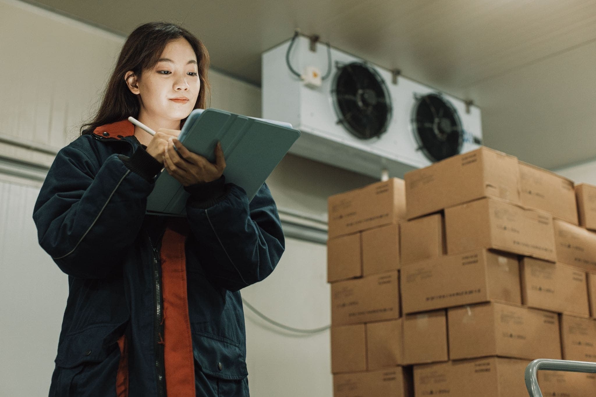 female worker performing inventory of boxes in a cold storage room in warehouse