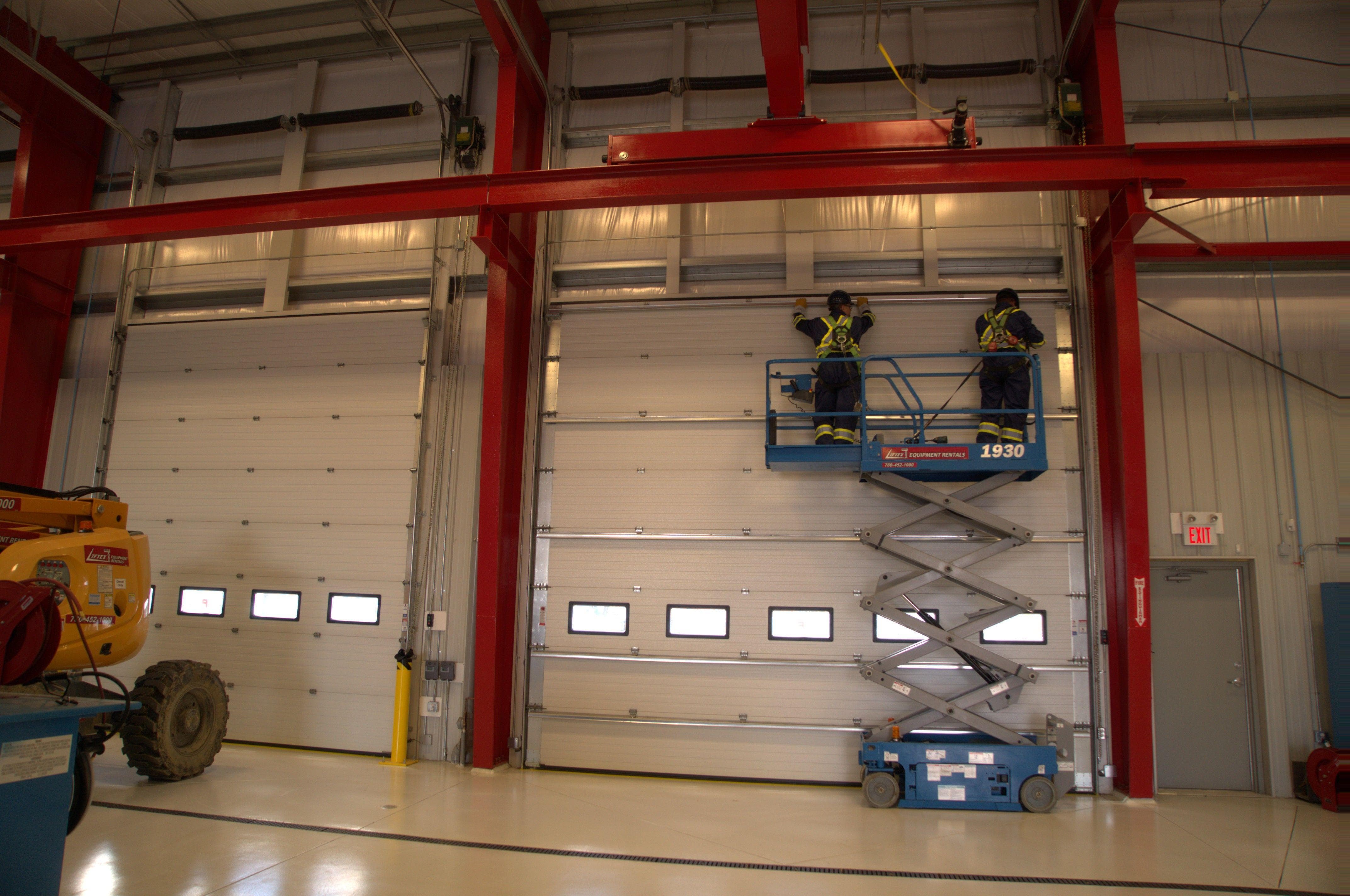 commercial technicians on a lift truck to inspect overhead door in warehouse