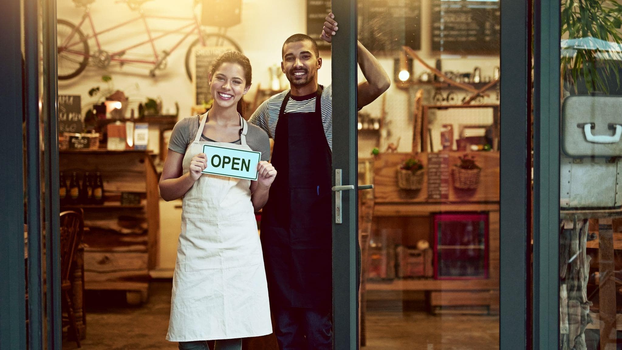 entrepreneurial couple standing in doorway to their shop holding an open sign