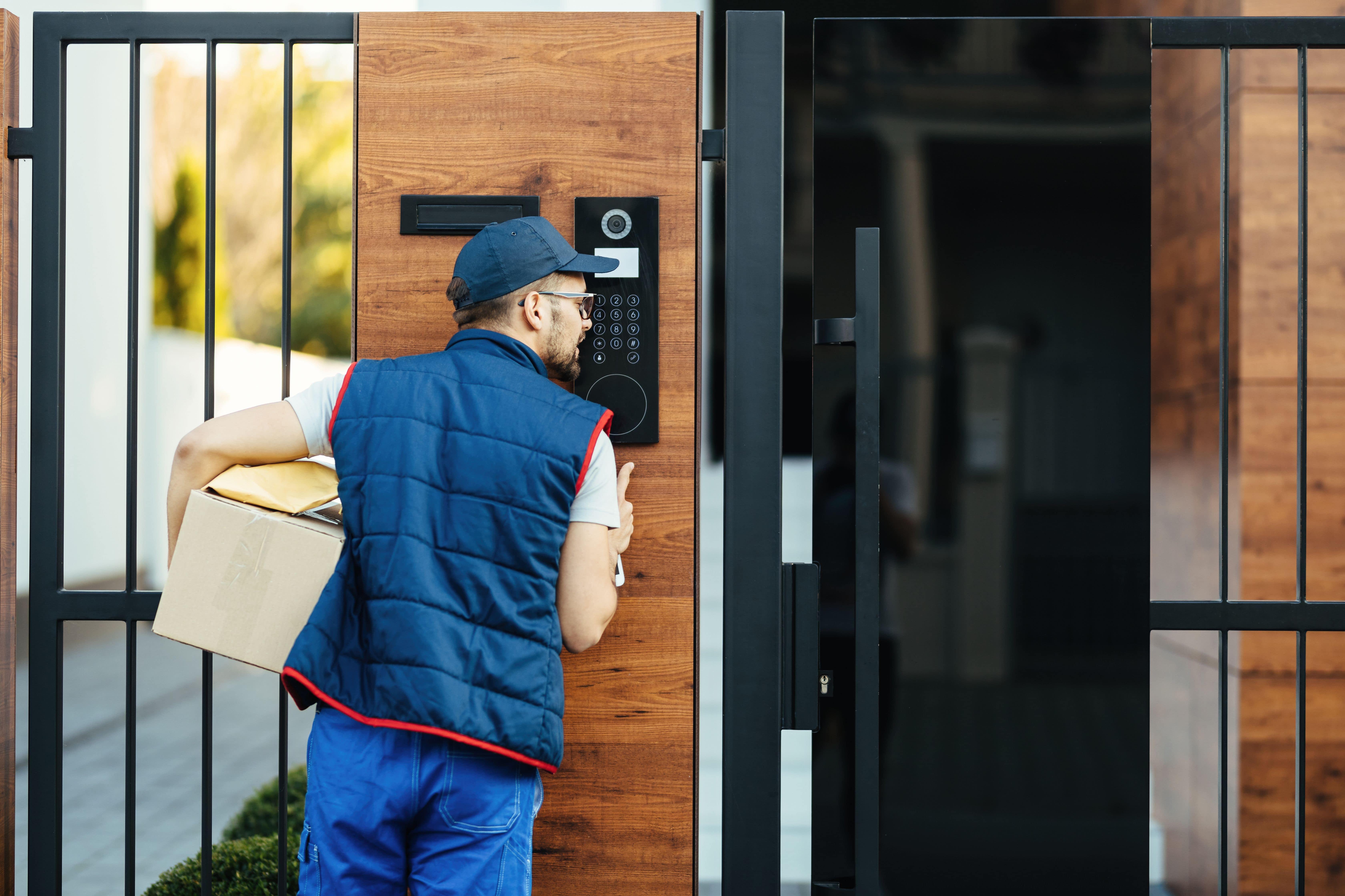 a delivery man using the wireless intercom on the gate to deliver a package