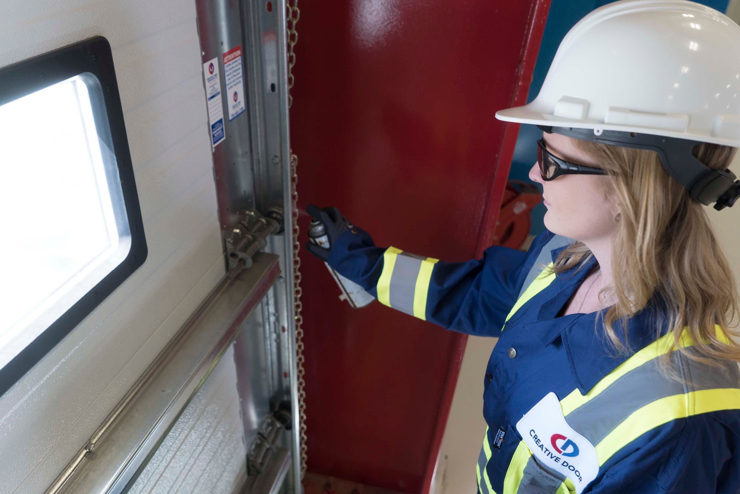 female creative door services technician performing maintenance on a sectional door