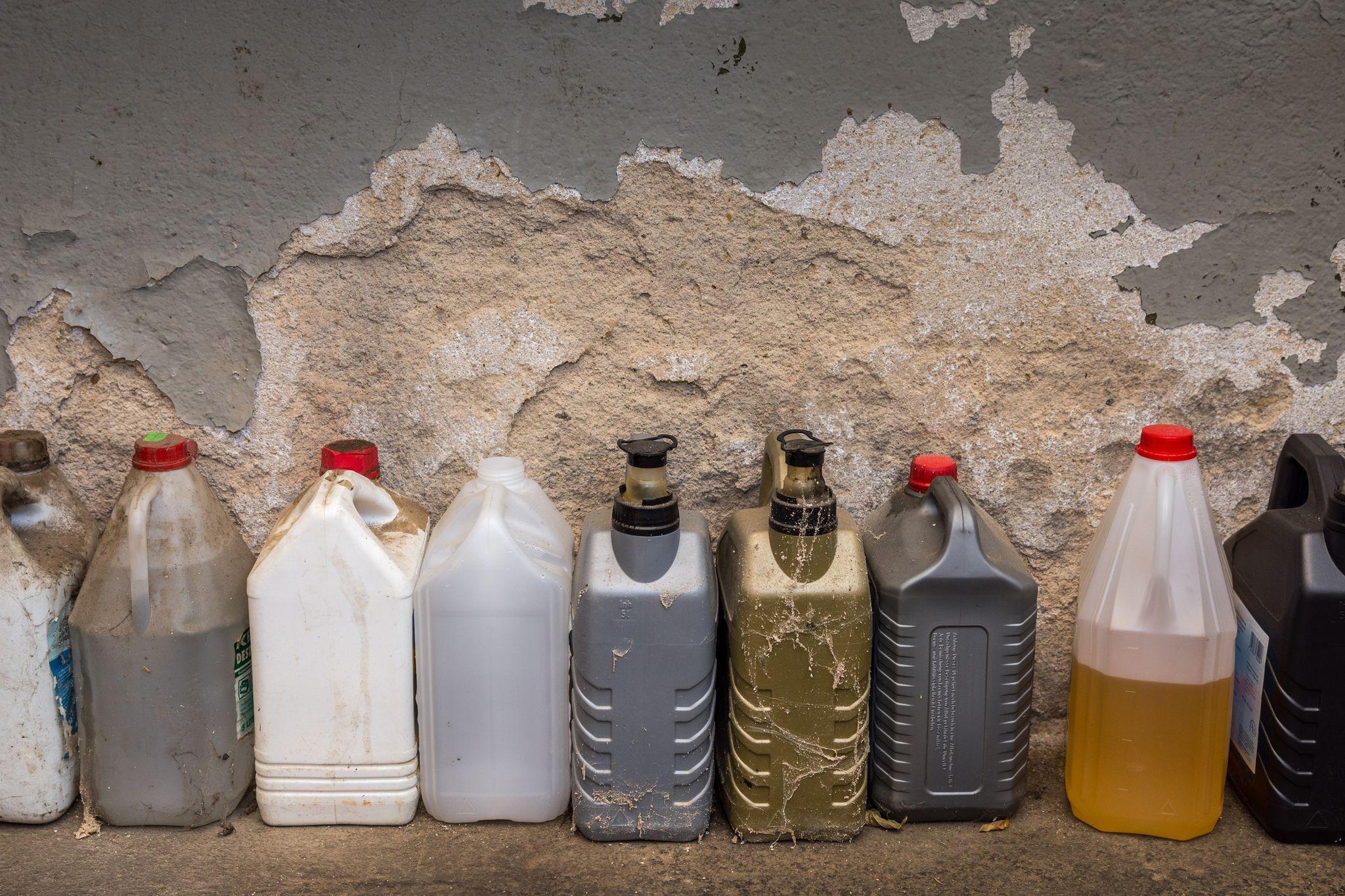 a row of dirty old containers in the garage containing hazardous chemicals and flammable agents