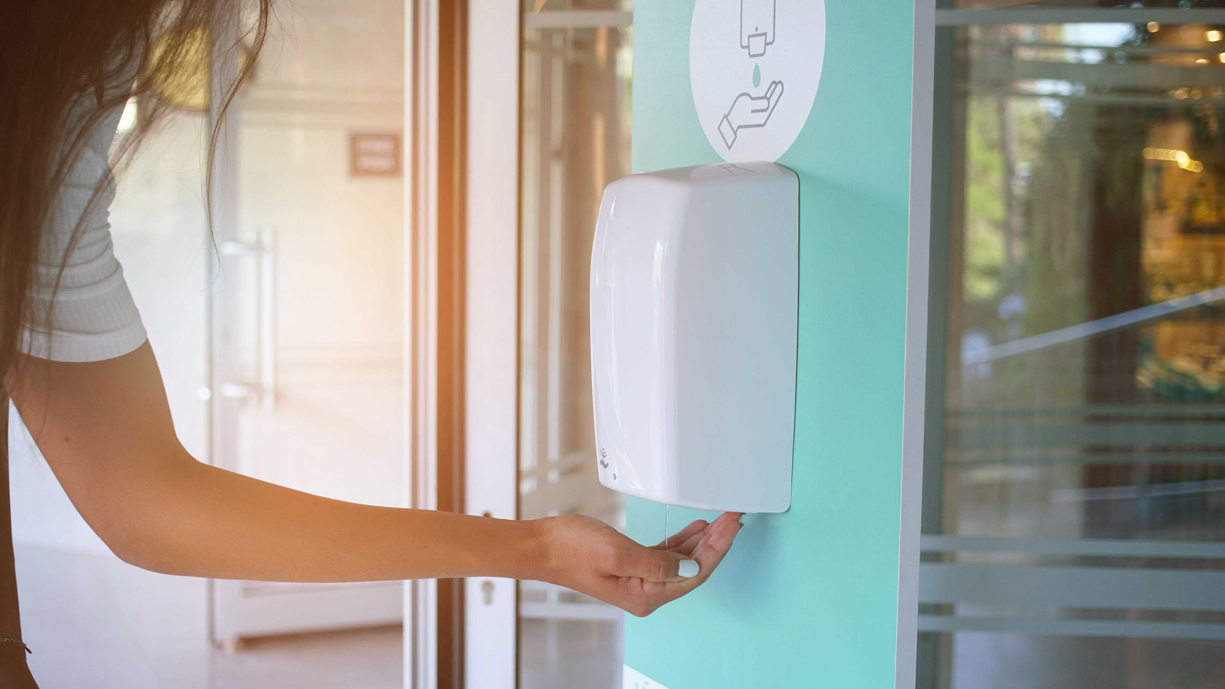 a woman using hand sanitizer at entry point of a building