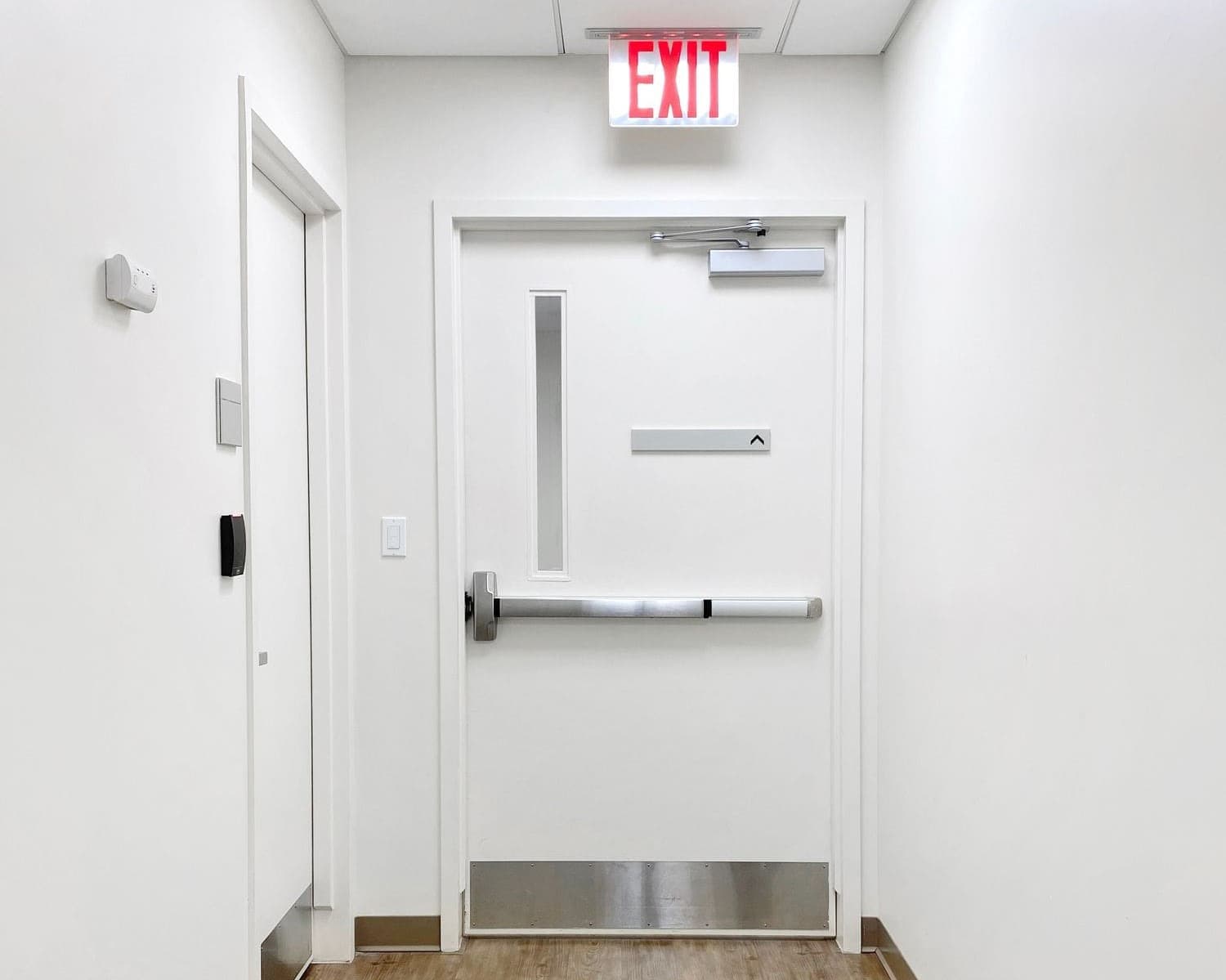 hospital corridor to emergency exit pedestrian man door with exit sign and pushbar