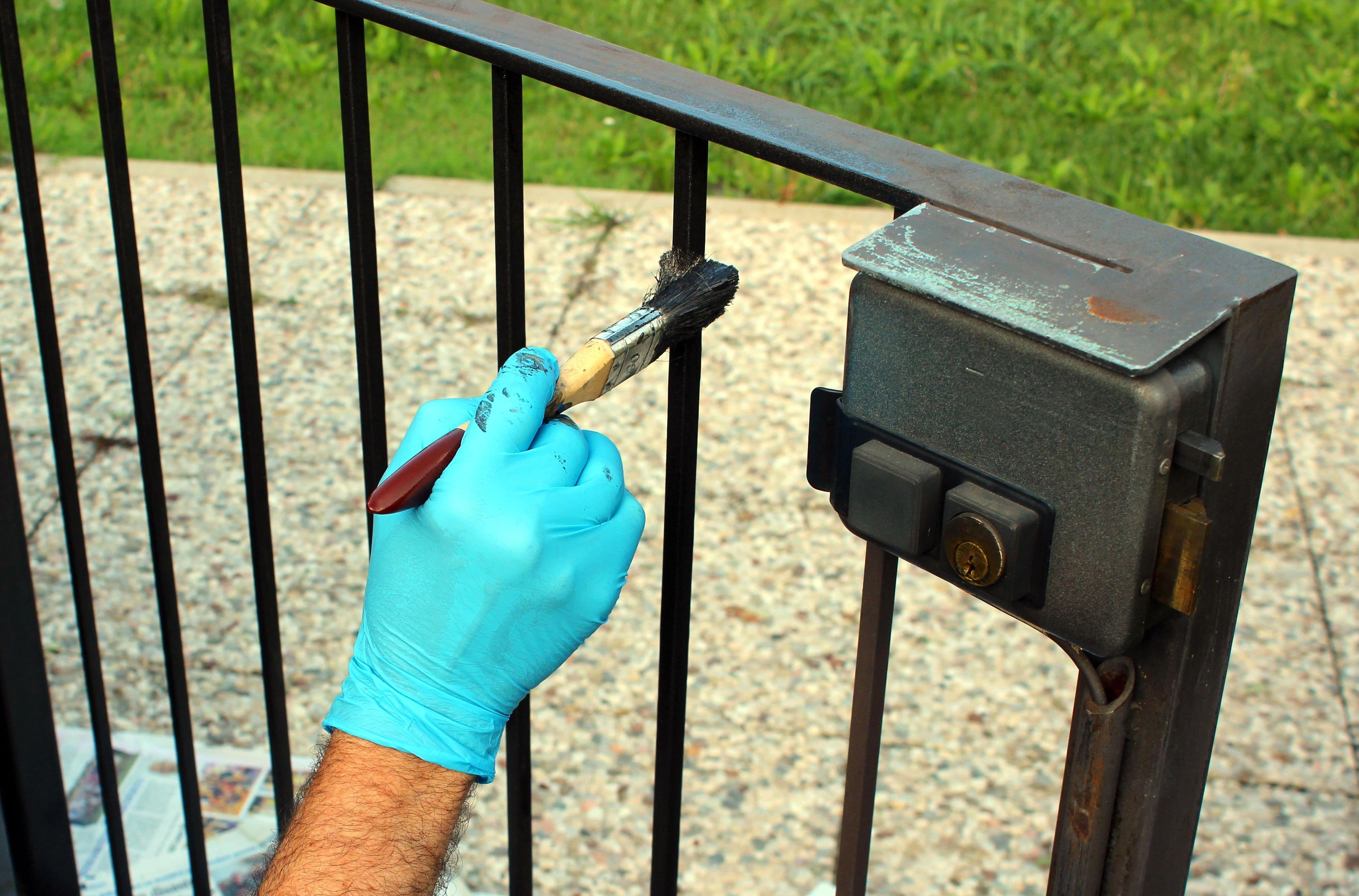 painter holding a brush re-applying fresh black paint to a wrought iron gate