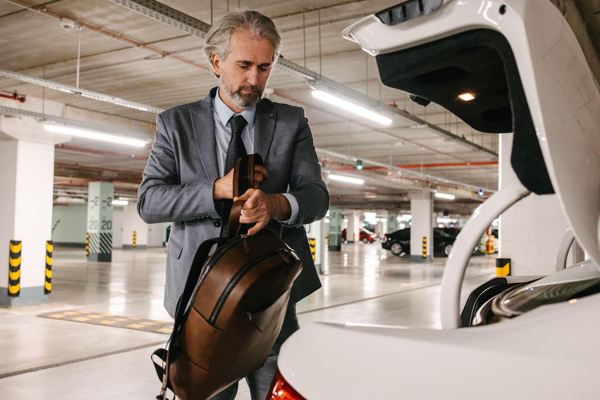 a businessman safely putting his leather bag in the trunk of his car