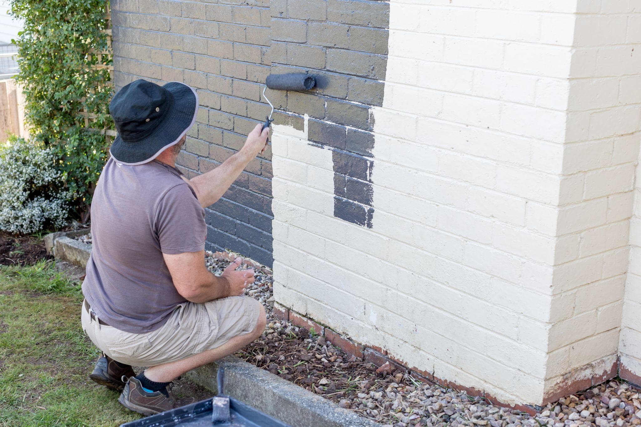 man painting exterior of brick home with charcoal grey paint