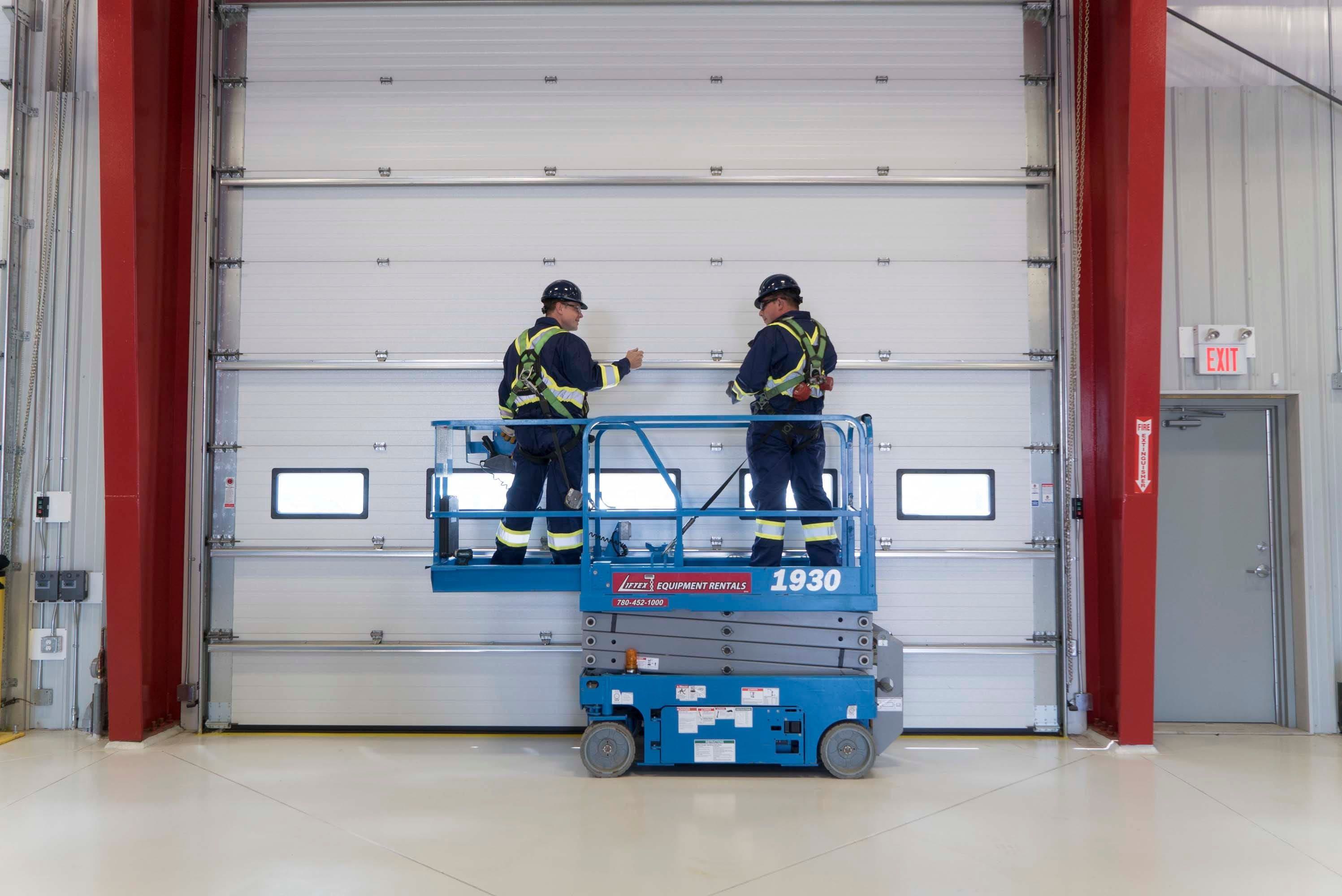 two creative door commercial technicians in a lift truck inspecting a sectional door