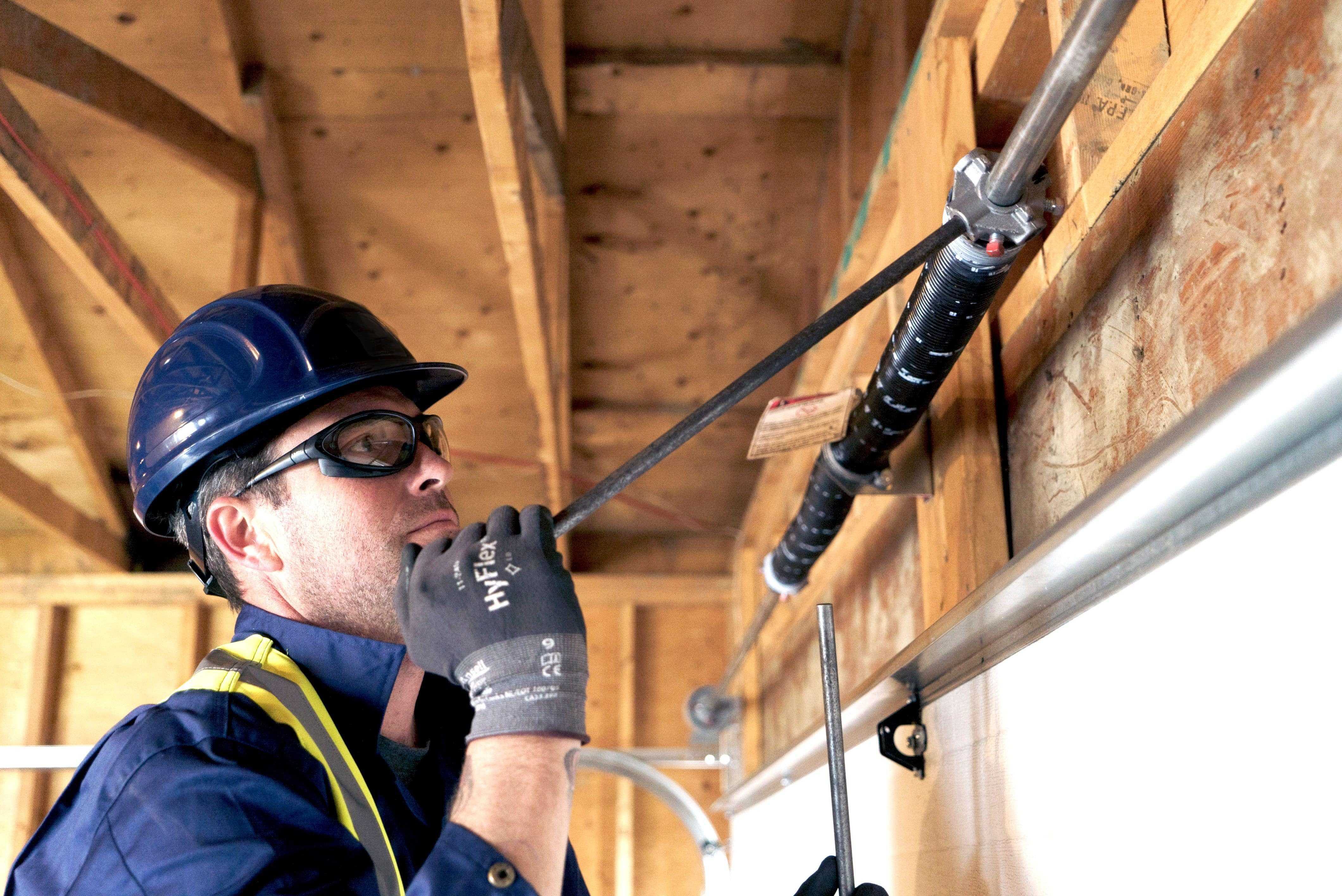 a creative door services technician carefully tightening a garage door spring