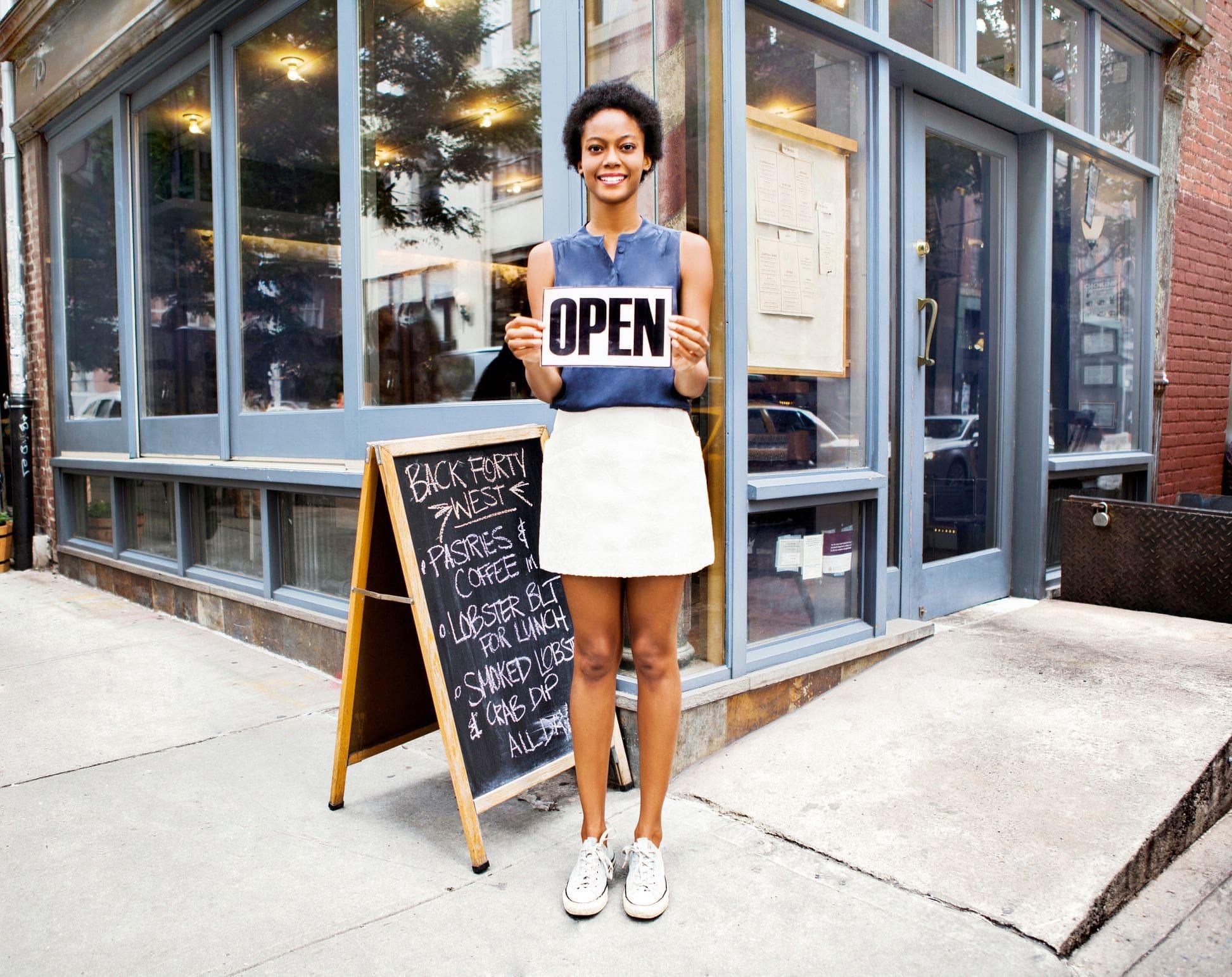 shop owner standing in from of commercial storefront with OPEN sign in summer shop owner standing in from of commercial storefront with OPEN sign in summer