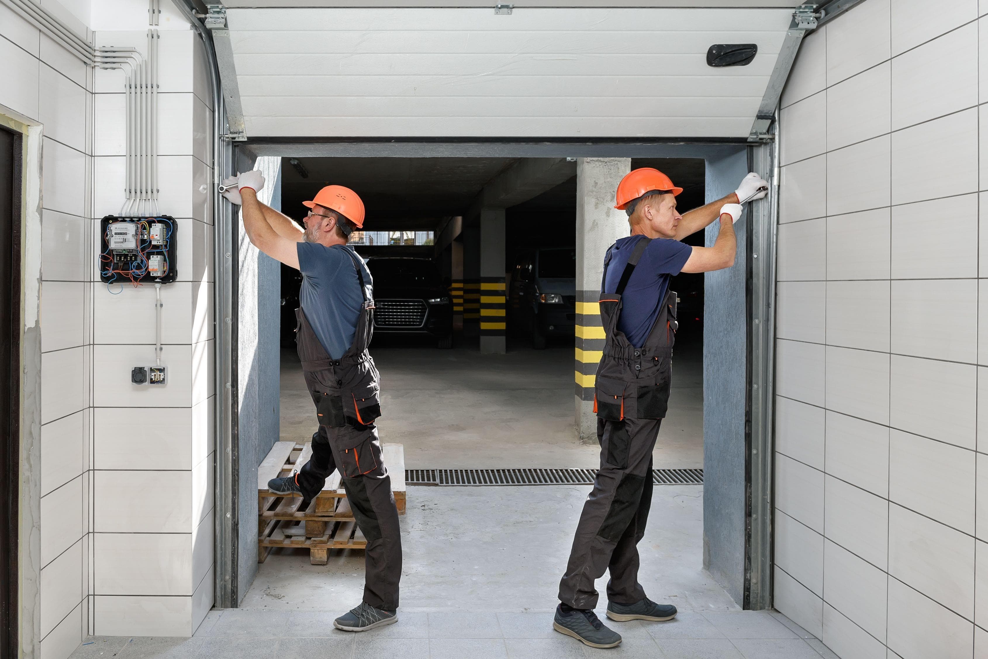 two technicians replacing garage door rollers in a parking garage
