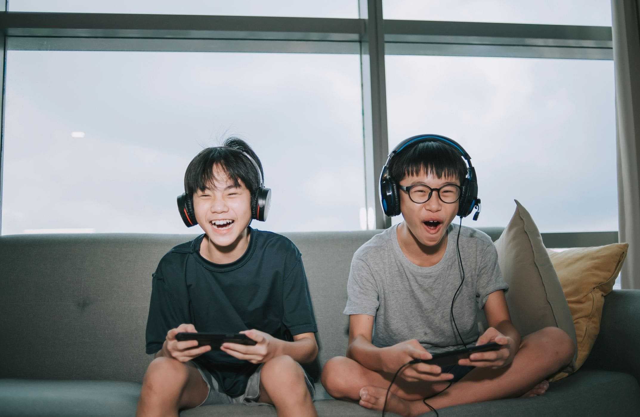two kids on couch laughing playing video games