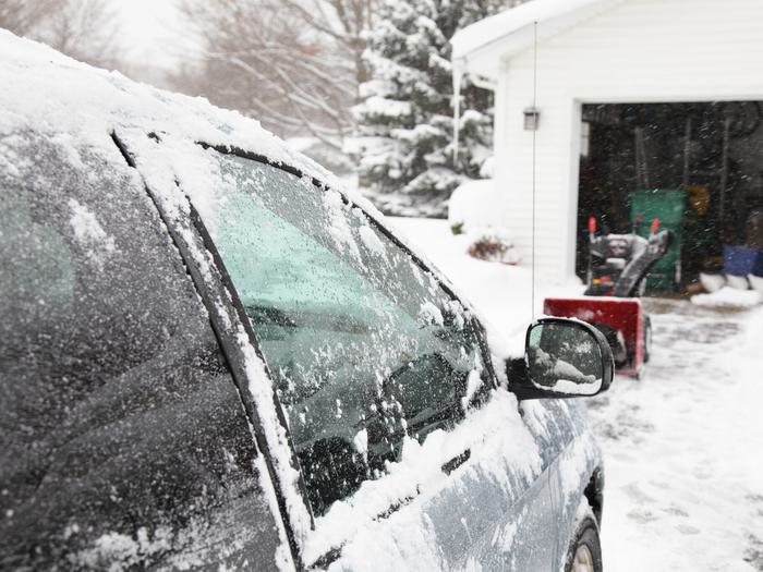 Car Covered In Snow Parked On A Snowy Driveway With Garage Door Opened